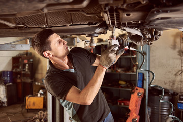 Repairman fixing car in garage. Experienced specialist car mechanic standing under lifted car...