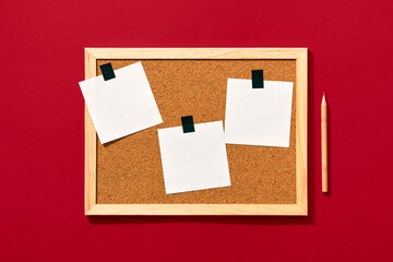 Cork board with wooden frame and three blank notes sticked on with black tape on red background,...