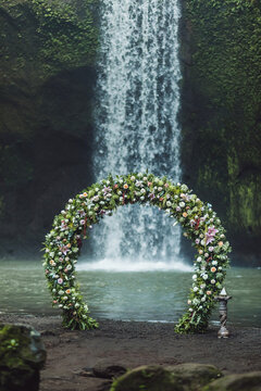 Wedding ceremony on Tibumana waterfall, Bali. Round arch with fresh flowers in jungle. Unusual nature wedding concept.