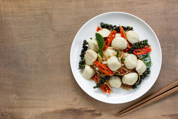 top view of stir fried sizzle fish ball in a ceramic dish on wooden table. asian homemade style food concept.