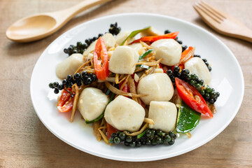 close up of stir fried sizzle fish ball in a ceramic dish on wooden table. asian homemade style food concept.