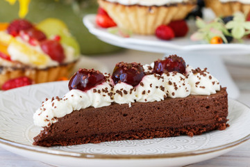 Chocolate cake with whipped cream decorated with cherries in a sweet sauce.