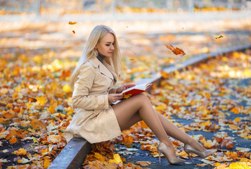 Student girl reading book in the autumn park.