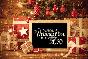 Blackboard With German Text Frohe Weihnachten Und Ein Glueckliches 2020 Means Merry Christmas And A Happy 2020. Christmas Tree With Decoration Like Ball, Gifts And Presents, Snowflakes