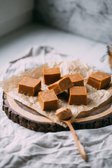Fresh caramel fudge candies on a wooden plate with copy space in marble background
