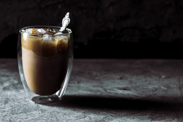 Pouring cream into a glass with iced coffee on table and black background