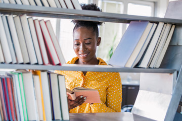 Education, high school and knowledge concept - African student woman with books over shelves in librarry. African american girl reading book in library