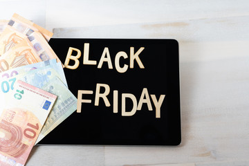The words Black Friday on the black screen of a tablet computer, next to some bills
