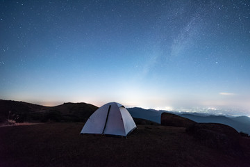 Tourist hikers tent in mountains at night with stars in the sky 