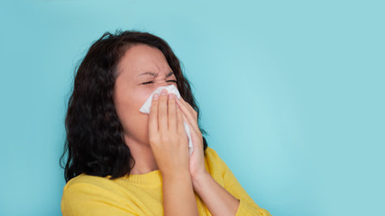 Young woman with cold blowing her runny nose. on a turquoise background