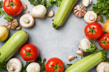 Set of different seasonal vegetables on a gray concrete background. Tomato zucchini onion garlic mushrooms parsley spices. Frame copy space.