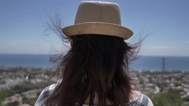 woman in a hat looks down on the city and the sea, back view, travel concept