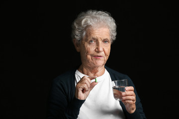 Elderly woman taking medicine on dark background