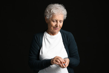 Elderly woman with pills on dark background