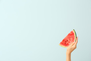 Female hand with piece of juicy watermelon on color background