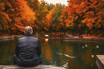 Alone man sits beside a pond in the park. Autumn background.