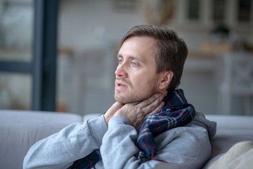 Blue-eyed man touching his neck while having tonsillitis