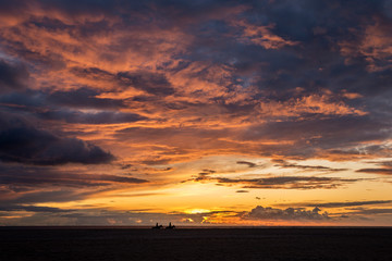 Horseback riding on Los Lances beach with a spectacular red cloud sunset in Tarifa, Cadiz province, Andalusia, Spain