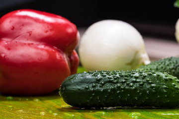 fresh vegetables with drops of water on a green wooden surface, poidor, cucumber, bell pepper, onion, greens, cauliflower