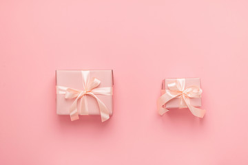 Holiday gift boxes with satin ribbon bow on a pastel pink background. Festive minimalism concept. Flat style layout.