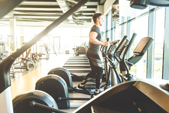 The athletic man dressed in a black sportswear running on the eleptic trainer in the modern gym