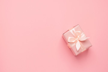 Festive gift box with satin ribbon bow on a pastel pink background. Festive minimalism concept. Flat style layout.