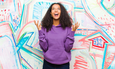 young pretty african american woman furiously screaming, feeling stressed and annoyed with hands up...