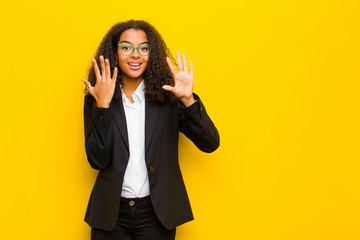 black business woman smiling and looking friendly, showing number ten or tenth with hand forward,...