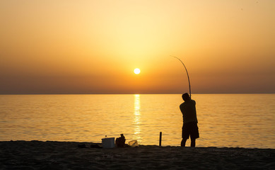 Fisher man fishing with spinning rod on black sea during sunrise