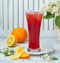 orange and lemon juice in tall glass with ice cubes in light background
