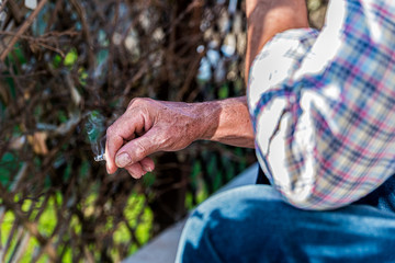Resting man's hand holding a cigarette against the background of the garden.