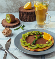 plate of pancake with spreaded chocolate and kiwi, ornage slices