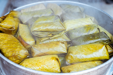 Close up view. Porridge rice wrapped in banana leaves pile in steamer with vapour smoke. Is traditional dessert found in rural areas of Thailand.