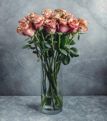 pale pink ombre rose bouquet in glass vase in front of grey wall