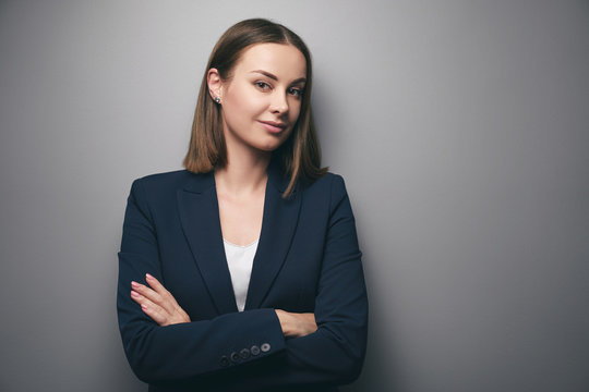 Confidence and charisma. Young business woman in suit looking at camera. Grey background.