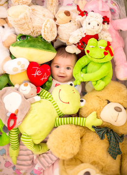 baby smiling lying camouflaged among stuffed animals and dolls and toys