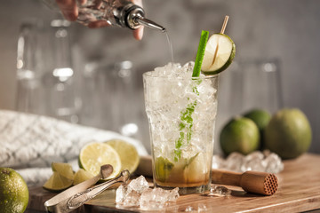 A glass of caipirinha on a wooden board with limes and crushed ice as decoration. A fresh traditional Brazilian cocktail with citrus fruits and rum.