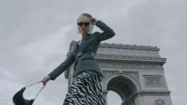 Outdoor autumn fashion portrait of elegant, luxury lady wearing trendy boucle blazer, zebra print pleated midi skirt, black sunglasses, holding baguette bag, posing near Triumphal Arch in Paris