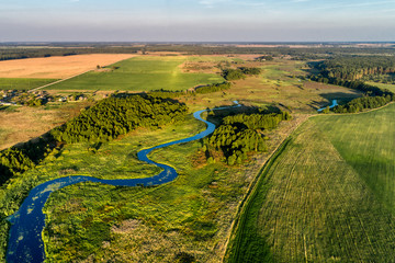 A small river flowing through meadows and agricultural fields. Aerial view. Evening shot with the setting sun.
