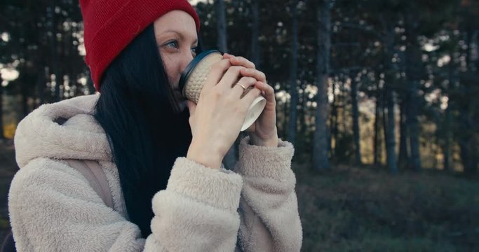 Young female smiling and drinking coffee. Pine forest. Mid shot.