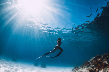 Attractive woman free diver glides with fins over sandy sea. Freediving in a tropical ocean