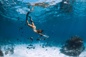 Young woman free diver in bikini glides over sandy sea with fishes. Freediving at Hawaii.