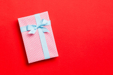 wrapped Christmas or other holiday handmade present in paper with blue ribbon on red background. Present box, decoration of gift on colored table, top view with copy space