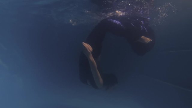 Woman is swimming in the dark water, doing backflip underwater, 4k
