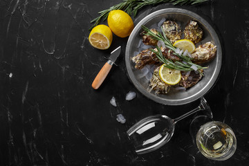 Fresh closed oysters, ice, lemon on a round metal plate and champagne are on a black stone textured background. Top view with copy space. Close-up.