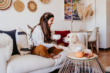 woman having a cup of tea at home during breakfast. Cute golden retriever dog besides. Healthy breakfast with fruits and sweets. lifestyle indoors