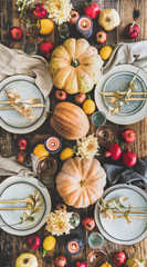 Fall table setting for Thanksgiving day or family gathering dinner. Flat-lay of plates, silverware, floral and fresh fruit decoration, candle and pumpkins over rustic wooden table background, top view