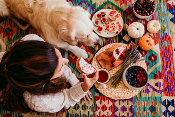 beautiful woman and cute golden retriever dog enjoying healthy breakfast at home, lying on the floor. healthy breakfast with tea, fruits and sweets. top view