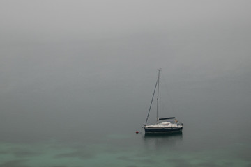 Sailboat sitting on a foggy lake in the morning.