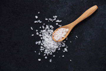 Crystal of white sea salt nd a wooden spoon on dark background